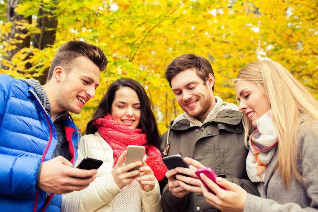 smiling friends with smartphones in city park