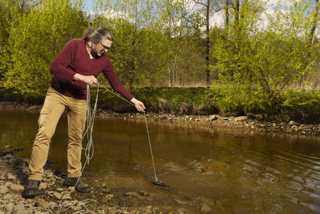 Exploring of river with magnet on rope by caucasian man