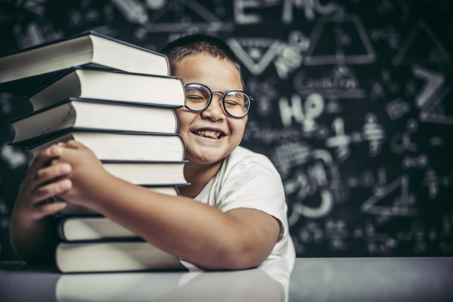A boy hugging a pile of books. Lese- und Rechtschreibförderung
