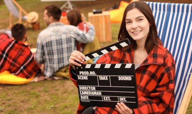 Happy young woman with movie clapper in outdoor cinema