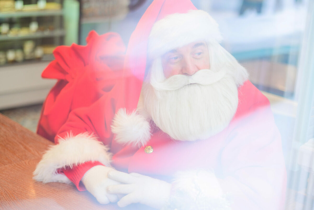 Santa Claus is sitting in a cafe. Outside view through the window.