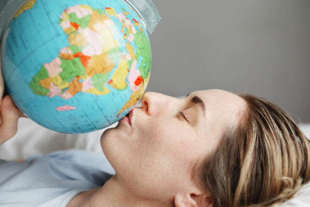 Portrait of young woman laying in bed and kissing globe. Horizontal.