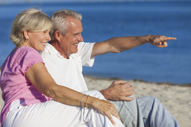 Senior Couple Sitting on Beach Pointing
