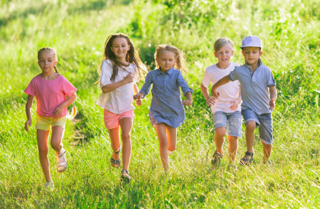 Kids, children running on meadow in summer's sunlight