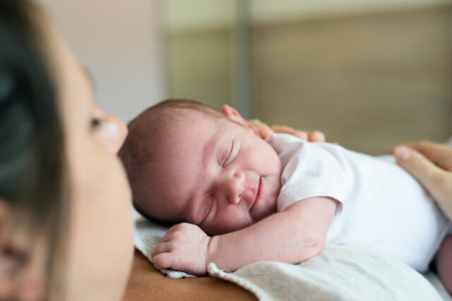 Unrecognizable mother with newborn baby son lying in bed