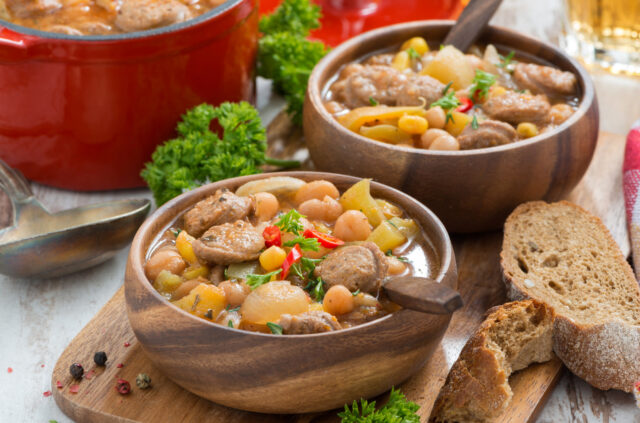 vegetable stew with sausages in a wooden bowl on board and bread