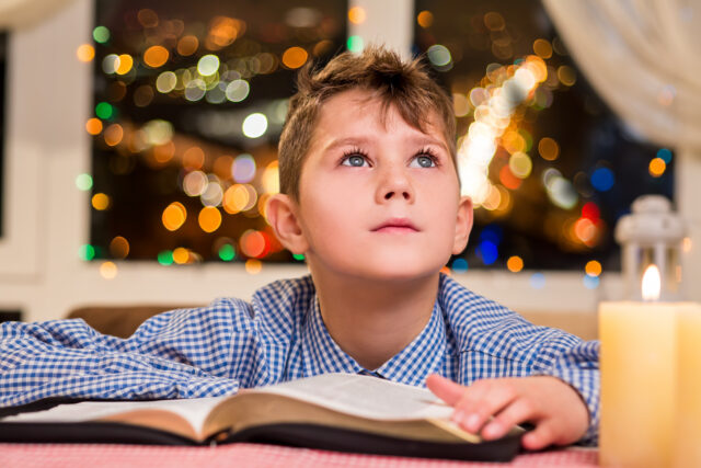 Kid with book near candle.