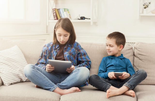 Two kids with gadgets on couch at home