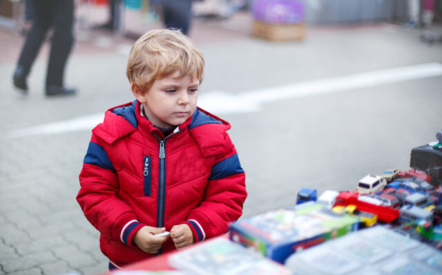 Beautiful toddler boy in red clothes on flea market.