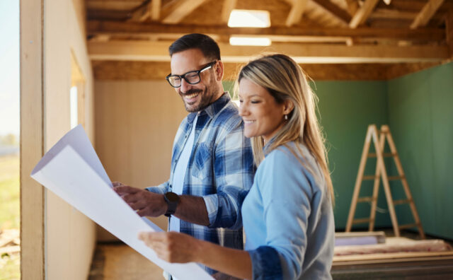 Happy couple reading blueprints of their developing house.