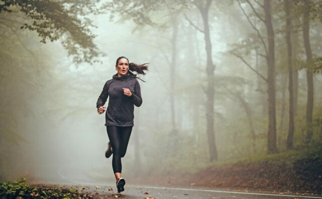 Young athletic woman jogging on the road in foggy forest.