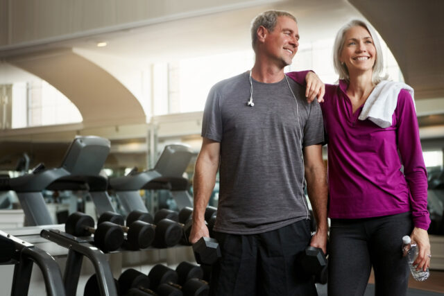 Senior couple, happy and break at gym, bottle and dumbbell for training, memory and exercise for health. Man, woman and smile together for support, workout and motivation with water at wellness club